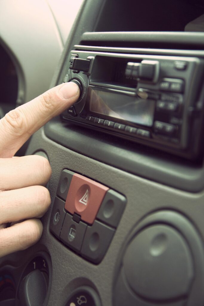 Finger adjusting car stereo in a vehicle's dashboard, depicting modern technology and music.